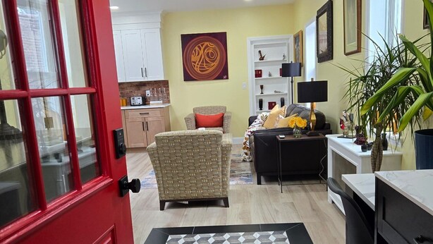 A modern living room with a red door, a patterned rug, a sofa, a coffee table, and a dining area with a white table and chairs. - The Hidden Gem (Saint Albans)