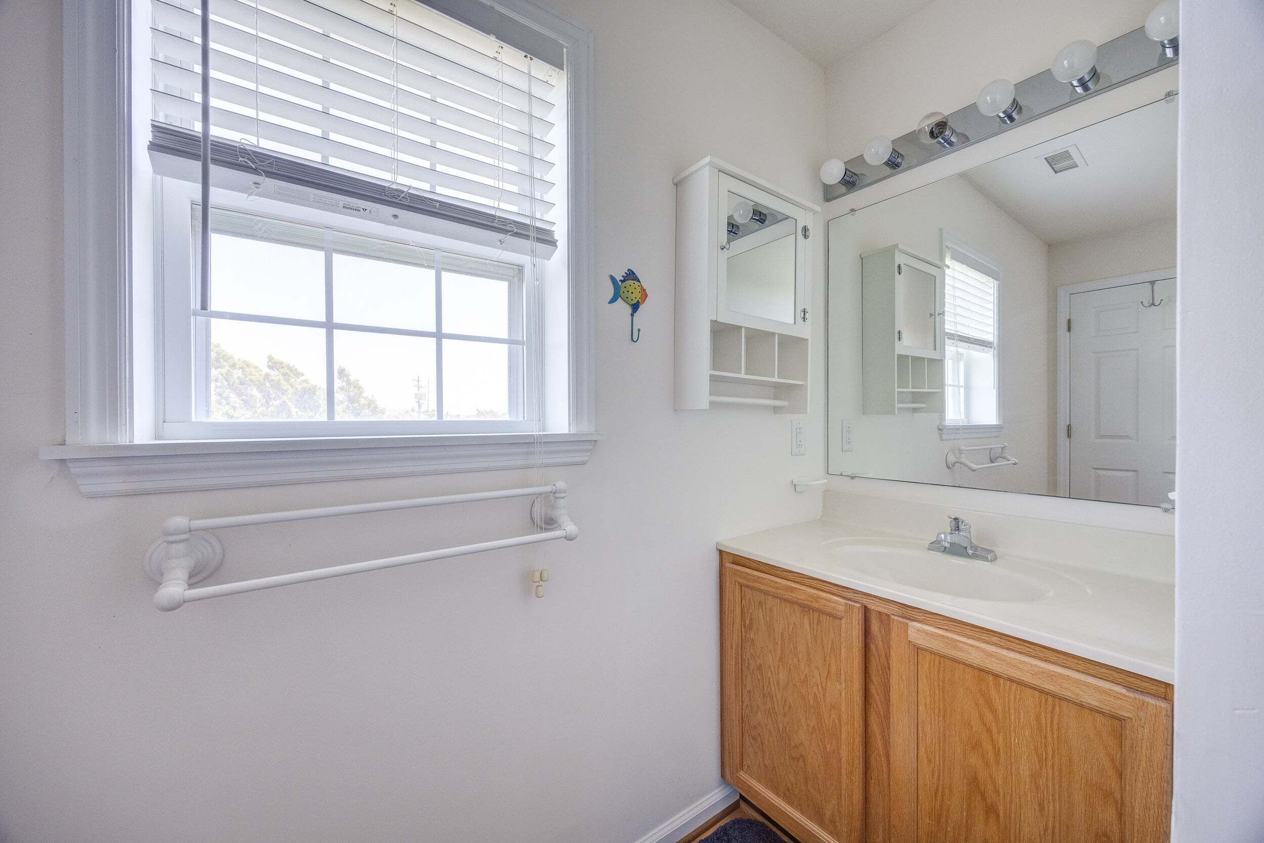 Une salle de bain avec une fenêtre, un lavabo, un miroir et des meubles en bois.
