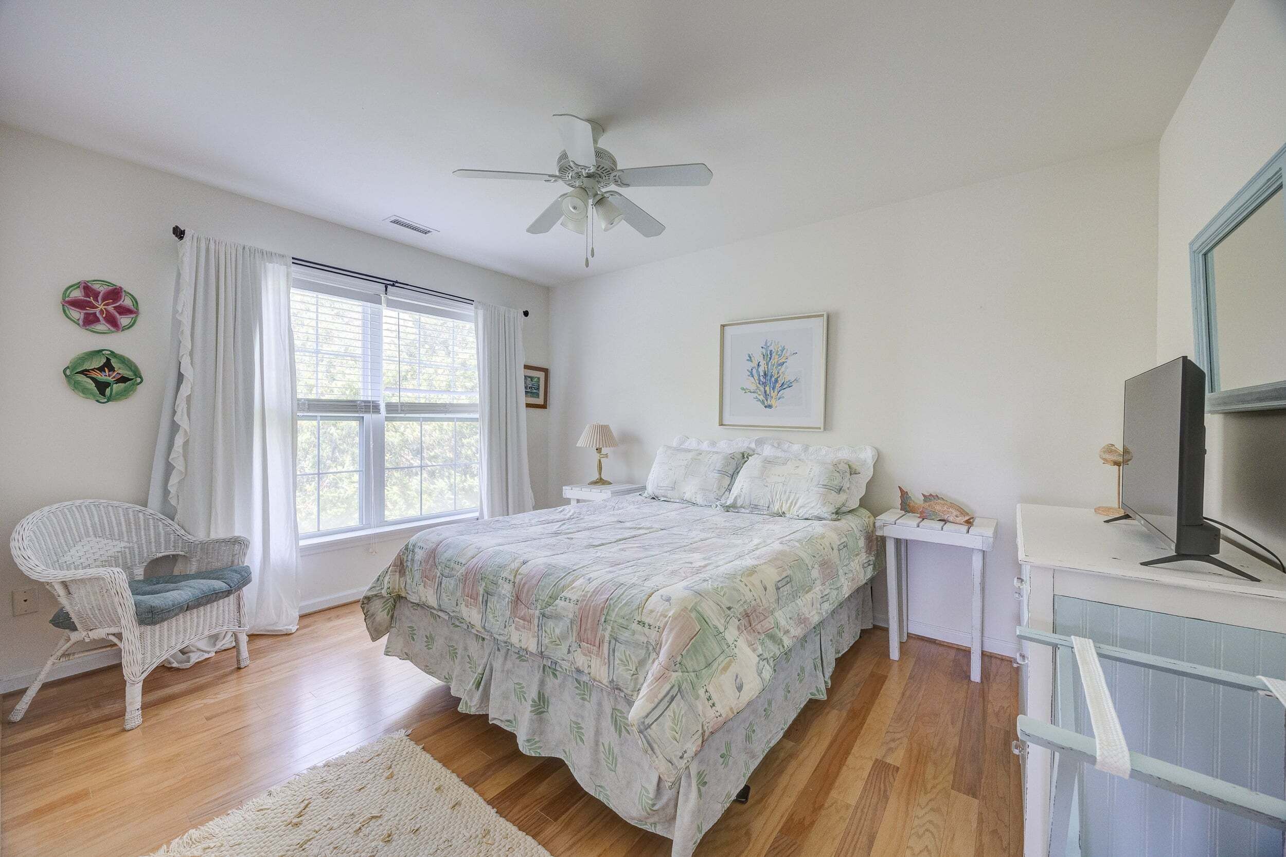 A bedroom with a bed, a chair, a desk, a television, and a ceiling fan.