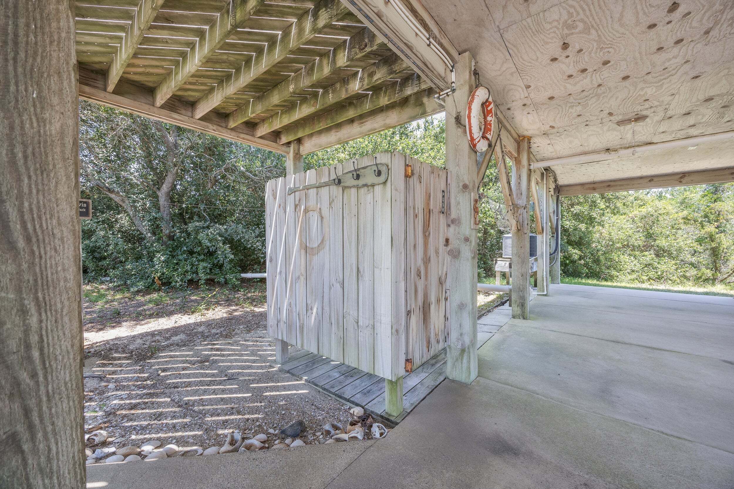 A covered outdoor area with a wooden structure, a concrete floor, and a stone pathway.