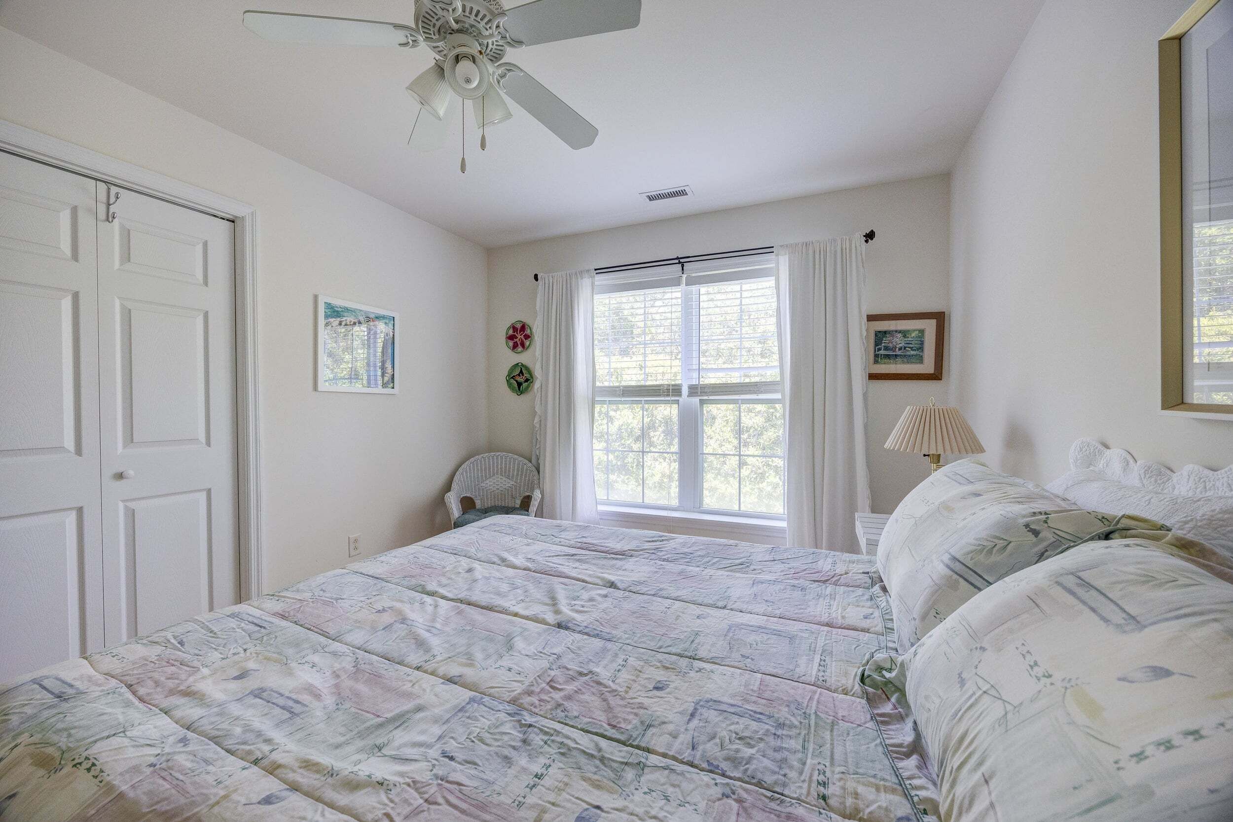 Une chambre à coucher avec un lit, un ventilateur de plafond, une fenêtre avec des rideaux et une porte.