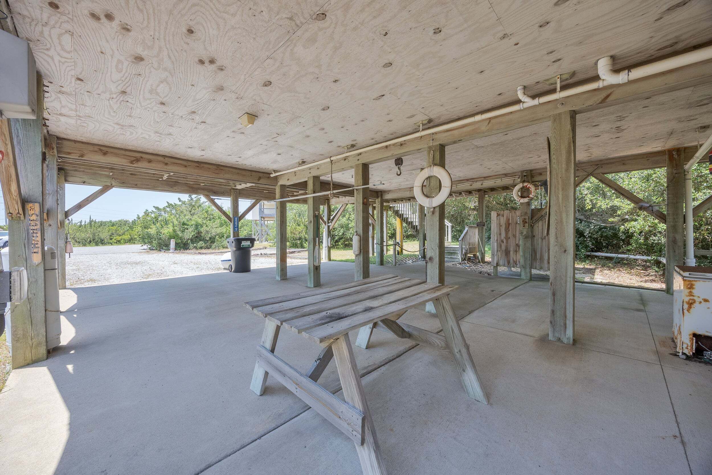 Une structure en bois installée à l’extérieur, dotée d’un sol en béton, d’un banc et d’une balançoire en forme de pneu suspendu.