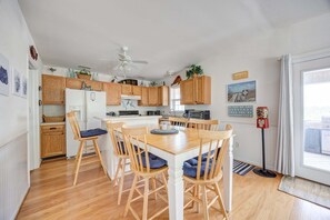 A kitchen with wooden cabinets, a white refrigerator, a dining table with chairs, and a ceiling fan. - 7630 - OBX BOX in Avon - Avon Beach Box | Classic OBX Getaway (Avon)