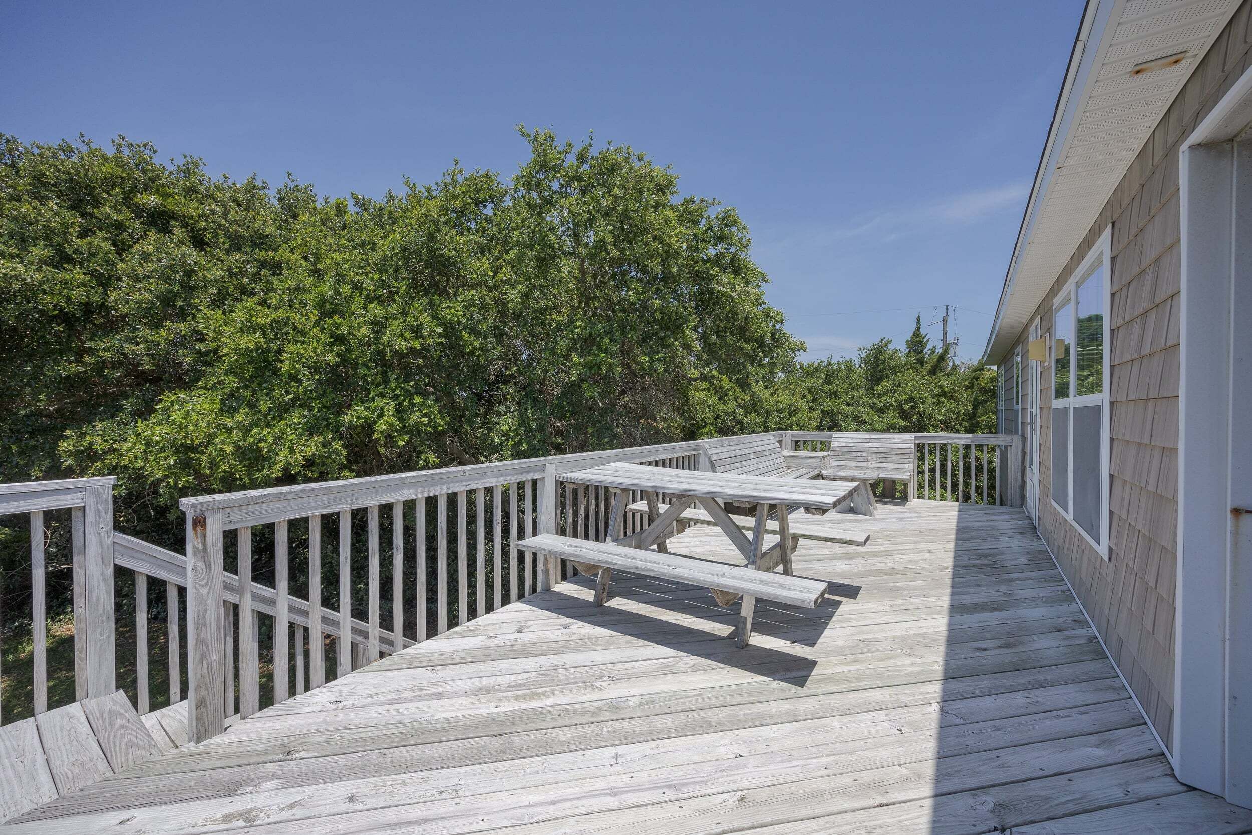 A wooden deck with picnic tables and a railing, surrounded by greenery.