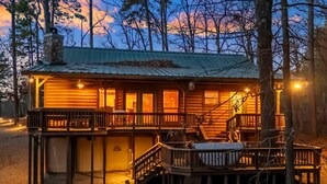 Eine rustikale Holzhütte mit Metalldach, einer Holzterrasse und einer Treppe, die zu einem Balkon führt.