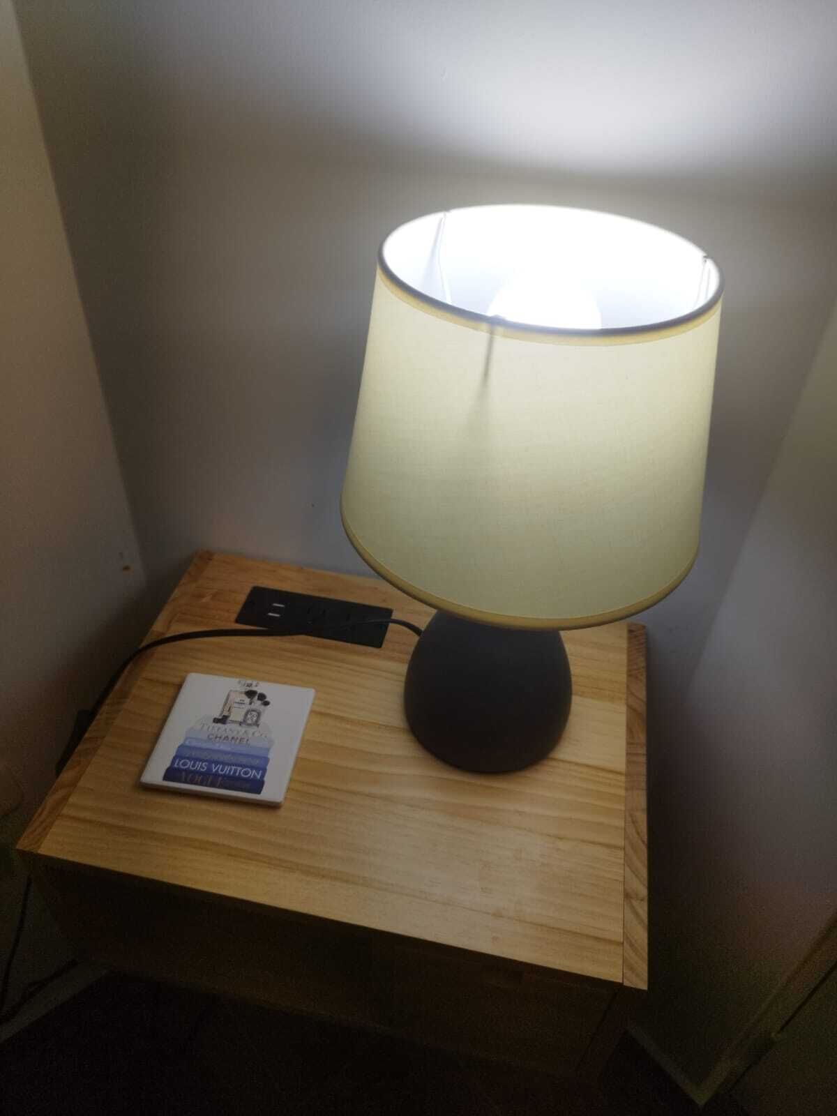 A bedside table with a lamp, a power strip, and a book titled "Louis Vuitton".