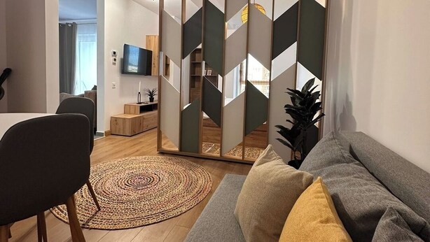 Un soggiorno moderno con un divano, una poltrona, un televisore e un pannello decorativo.