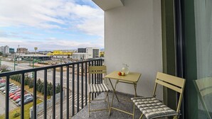 Un balcone con tavolo e due sedie, affaccia su un parcheggio e sulla città.