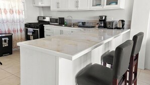 A kitchen with white cabinets, a central island with bar stools, a stove, microwave, and a coffee maker. - 2BR Oceanview • Walk to Beach • Saint Lucia (Vieux Fort)