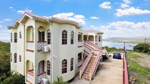 A large, multi-story house with a balcony, a staircase, and a view of a body of water. - 2BR Oceanview • Walk to Beach • Saint Lucia (Vieux Fort)
