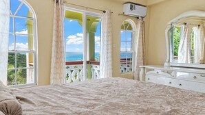 A bedroom with a large bed, a dresser, and a window with a view of the sea. - 2BR Oceanview • Walk to Beach • Saint Lucia (Vieux Fort)