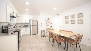 Une cuisine moderne avec des meubles blancs, des appareils en acier inoxydable et une table à manger en bois, accompagnée de chaises.