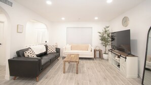 Un salon moderne avec un canapé noir, un canapé blanc, une table basse en bois, un téléviseur posé sur un meuble en bois et une plante en pot.