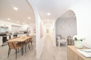 A modern kitchen with white cabinets, a dining area with a wooden table and chairs, and a hallway with a white sofa and decorative plates on the wall. - Family-Friendly Home - Space for Everyone - Dog Friendly! (Phoenix)