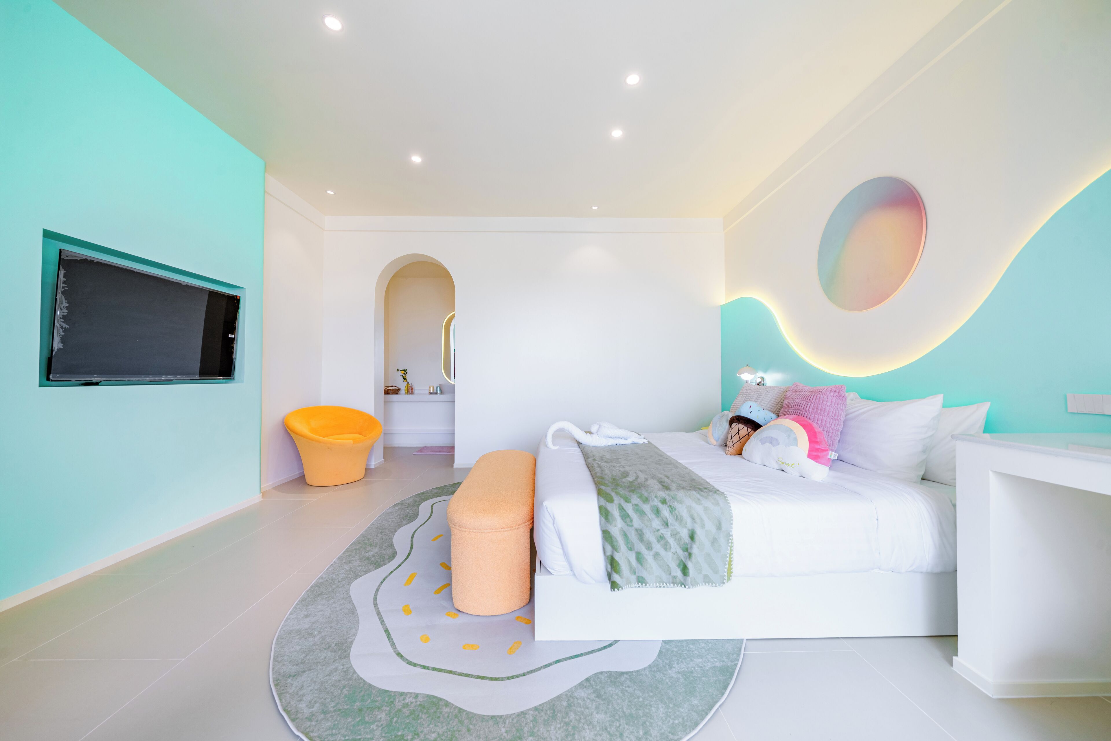 A modern bedroom with a bed, a small stool, a round rug, and a television mounted on the wall.