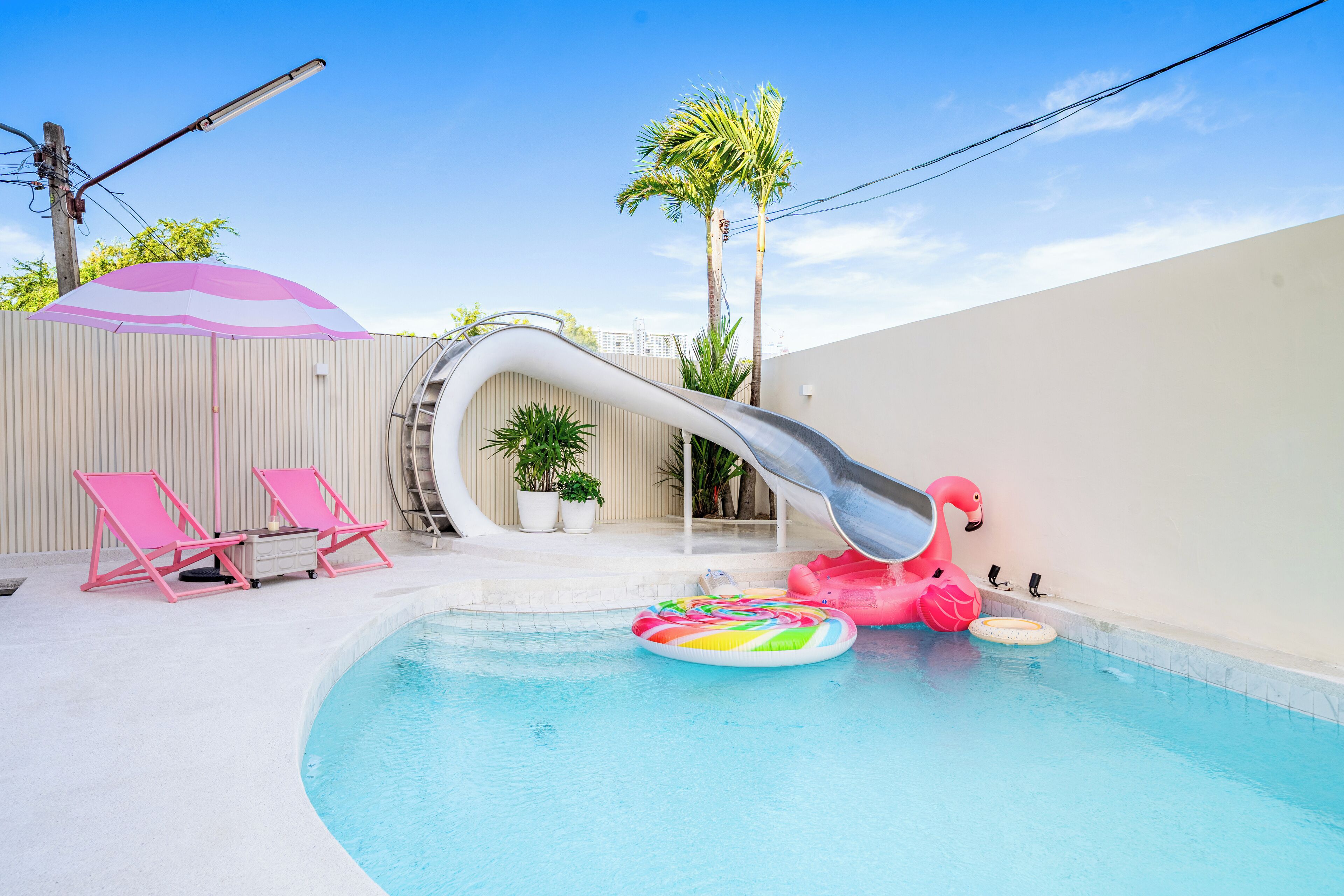 A swimming pool with a slide, pink flamingo floaties, and lounge chairs.