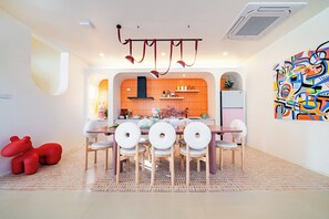A modern kitchen with a central island, wooden chairs, and a colorful abstract painting. - Candy House Pool Villa with KTV (Pattaya)