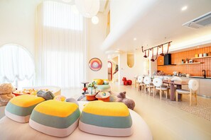 A bright living room with a large window, a dining area with a table and chairs, and a kitchen with orange tiles. - Candy House Pool Villa with KTV (Pattaya)