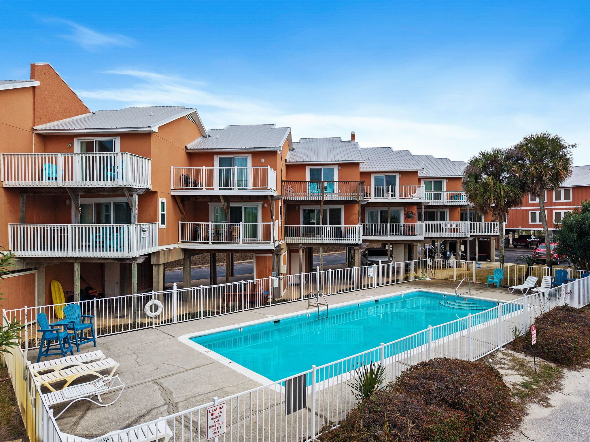 A row of two-story buildings with balconies, a swimming pool, and lounge chairs.