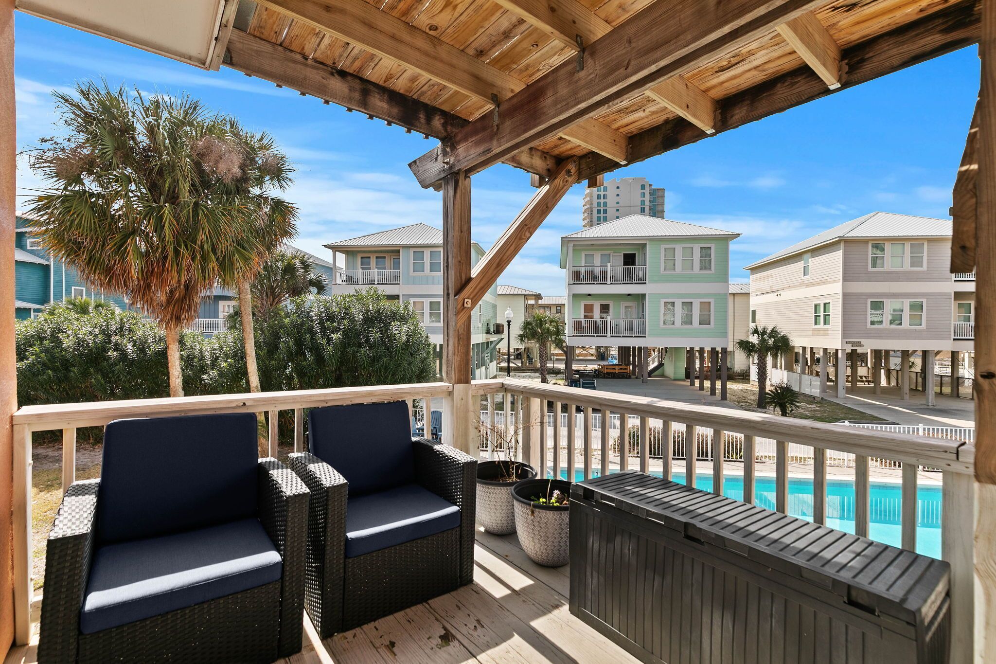 Eine Holzterrasse mit Korbmöbeln, einem Pool und Gebäuden im Hintergrund.