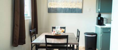 Een eethoek met een houten tafel, stoelen, een vaas met bloemen en een schilderij aan de muur.