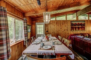 A wooden cabin interior with a dining table set for four, a sofa, and a painting on the wall. - Is today a Lake or Links kind of day? Now booking for Summer 2026! (Breezy Point)