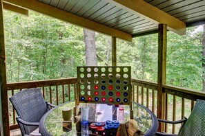 A covered deck with a table and chairs, a pegboard game, and a view of a forest. - Is today a Lake or Links kind of day? Now booking for Summer 2026! (Breezy Point)