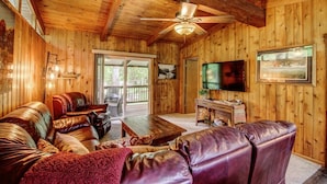 A wooden interior with a ceiling fan, leather sofas, a TV, and a sliding glass door leading to an outdoor area.