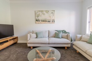 Un salon avec un canapé beige, une table basse et un téléviseur posé sur un meuble en bois.