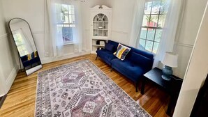 A living room with a blue sofa, a patterned rug, a ceiling fan, and a large mirror.