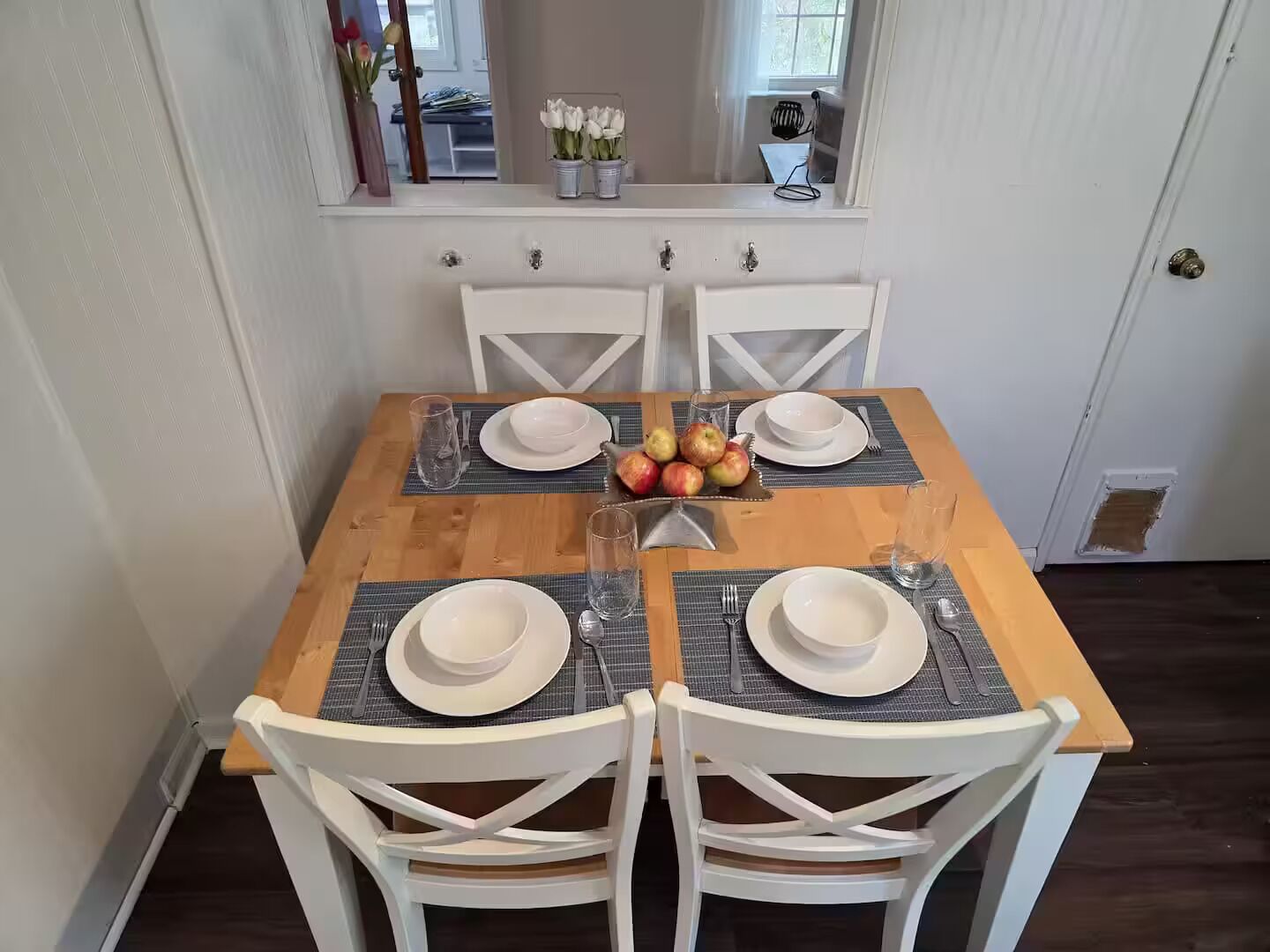 A dining table set with white plates, bowls, and cutlery, surrounded by white chairs.