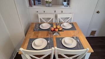 A dining table set with white plates, bowls, and cutlery, surrounded by white chairs.
