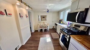 A kitchen with white cabinets, a microwave, stove, and a dining area with chairs and a table.