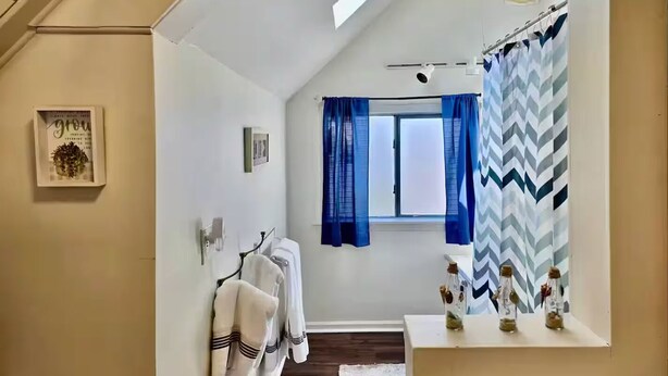 A modern bathroom with a skylight, a shower curtain with a chevron pattern, and a small shelf with decorative items.
