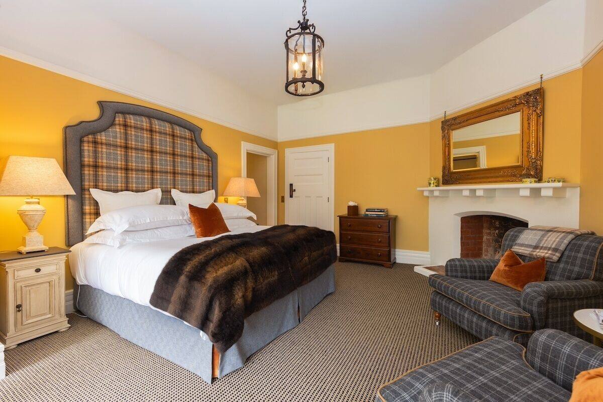 A hotel room with a bed, a sofa, a fireplace, a mirror, and a chandelier.