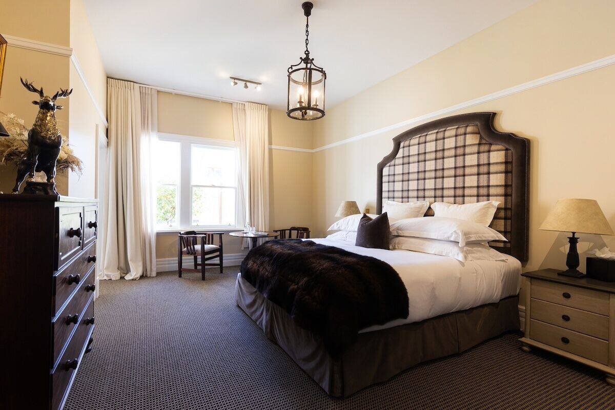 A hotel room with a large bed, a desk, a chair, a dresser, and a chandelier.