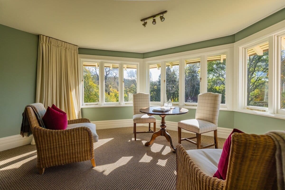 A room with a large bay window, wicker furniture, a round table, and a patterned carpet.