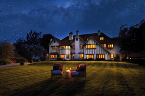 Une grande maison avec de nombreuses fenêtres et une pelouse bien éclairée la nuit.