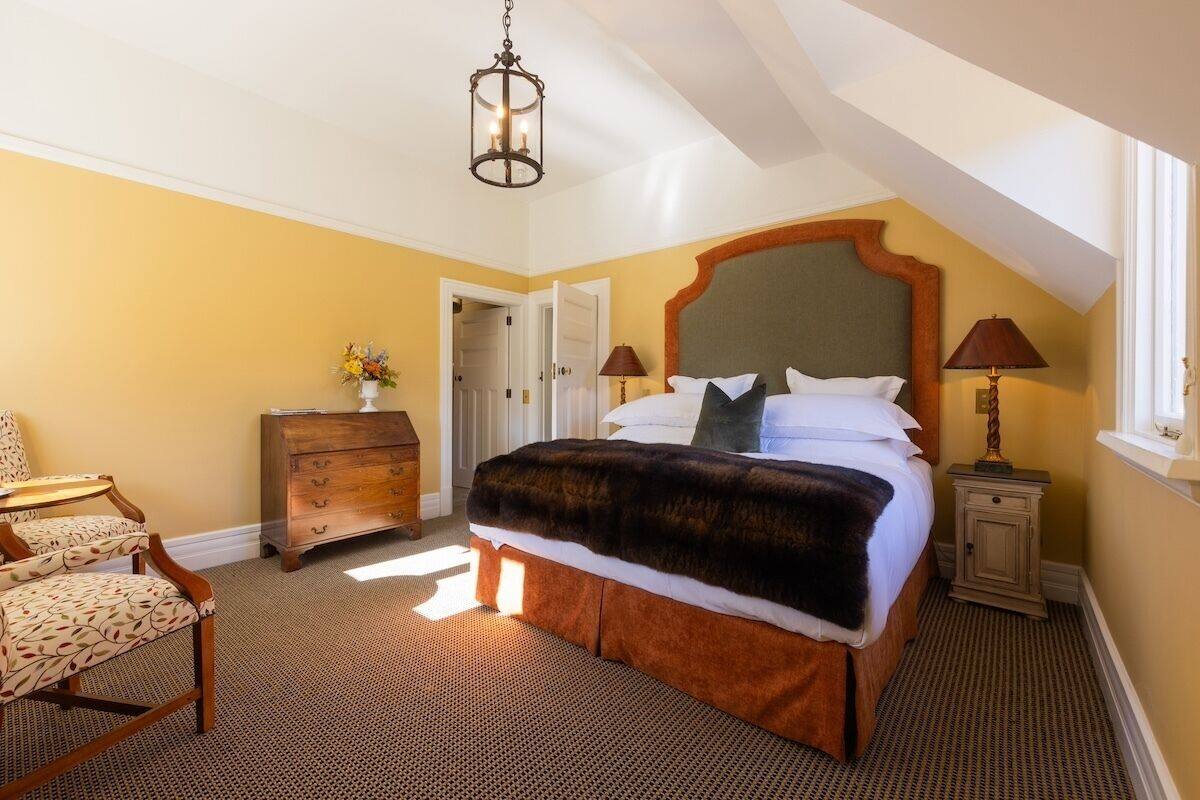 A bedroom with a large bed, a dresser, a chair, and a lamp.