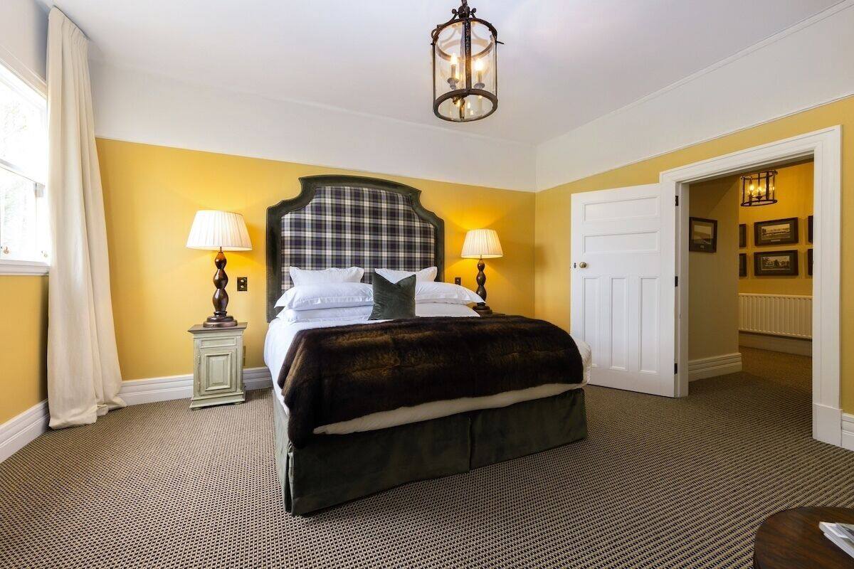 A hotel room with a large bed, two bedside lamps, a headboard, and a chandelier.