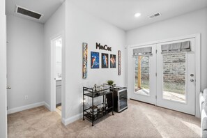 A hallway with a white door, a glass door leading outside, and a black metal shelf with various items.