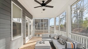 Une véranda abritée avec un canapé, un pouf et un ventilateur de plafond.