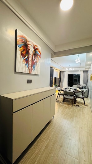 A modern kitchen with a dining area, a large painting on the wall, and a view into the living room. - Kilimani Sky Retreat - 2BR Epic Panoramic Views (Nairobi)