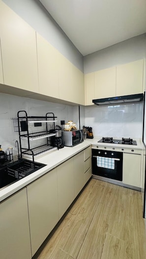 A modern kitchen with white cabinets, a black sink, a stove, and a microwave. - Kilimani Sky Retreat - 2BR Epic Panoramic Views (Nairobi)