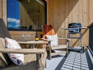 Une terrasse en bois avec une table, des chaises, une bouteille de vin et un barbecue.