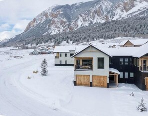 Un quartier résidentiel enneigé, avec des maisons, un paysage montagneux en arrière-plan et un ciel dégagé.