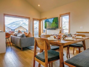 A dining area with a wooden table set for four, a sofa with cushions, and a television mounted on the wall. - Scandinavian Condo w/ Mountain Views & Free Parking (Crested Butte)
