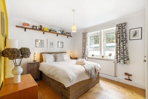 Une chambre à coucher avec un lit en bois, des tables de chevet, une fenêtre avec des rideaux, une étagère remplie de livres et des tableaux encadrés accrochés au mur.