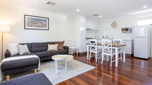 A modern apartment with a grey sofa, white dining table, and chairs, a kitchen with white cabinets, and a white refrigerator. - Hidden Gem - Fremantle Apartment (Fremantle)