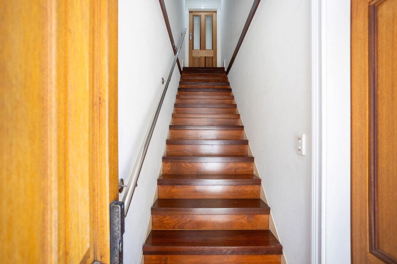 A wooden staircase with a handrail leading to a door at the top.